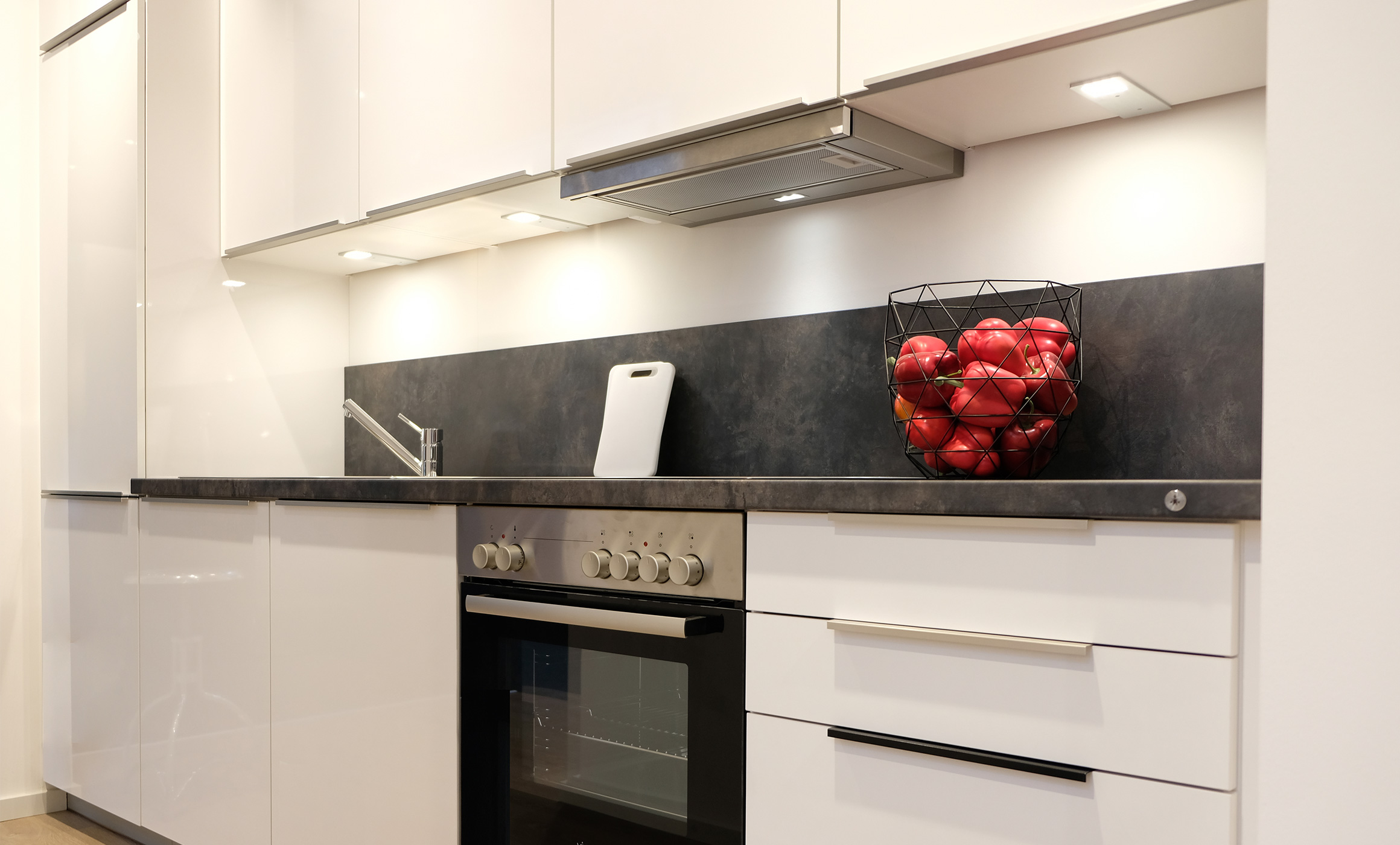 Weiße Küchenzeile in hochglanz mit Oberschränken und Hochschrank in der Hummel Küchenwerk Ausstellung.