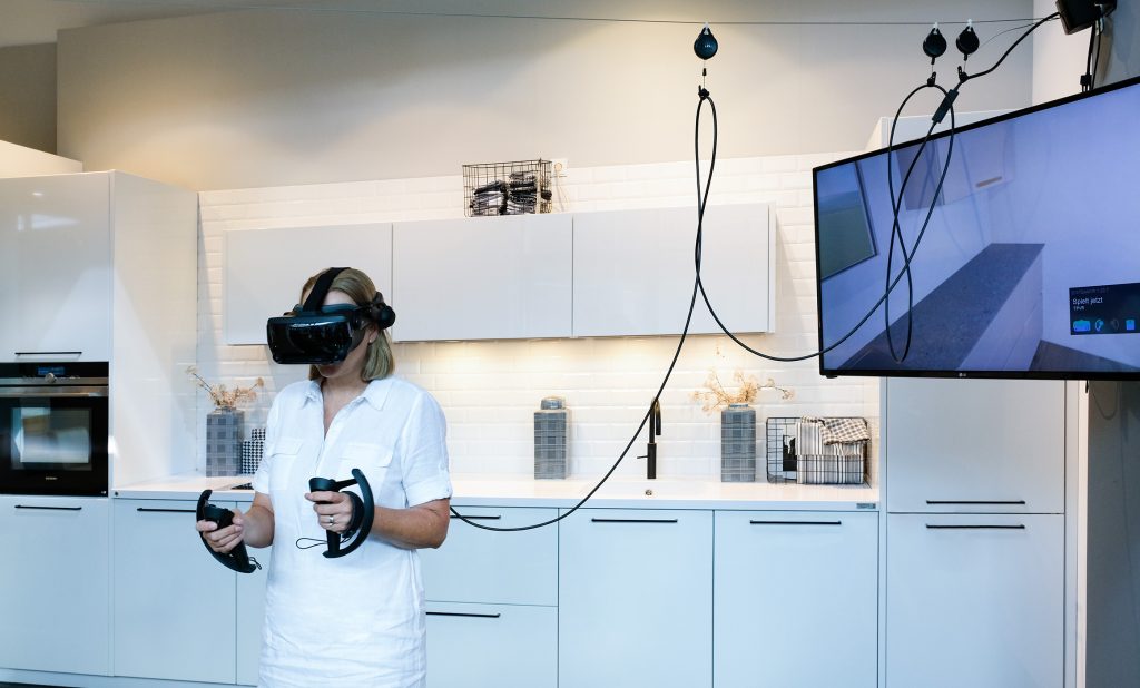 Frau mit VR-Brille agiert mit Controler in Küche Bildschirm mit Küchenplanung 3D Erlebnis