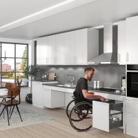 Weiße, barrierefreie Küchenzeile im offenen Wohnraum. Alles optimal im Zugriff für den Rollstuhlfahrer. Hummel Küchenwerk.